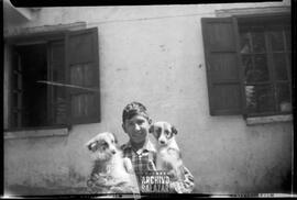 Niño no identificado posando con dos perros frente a cámara.