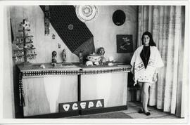 Mujer junto a exposición de artículos folclóricos ecuatorianos de la Organización Comercial Ecuatoriana de Productos Artesanales (OCEPA).
