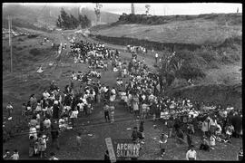 Canal 6 TV, Primera Maratón, 1961. Panorámica de fila de niños y algunos adultos que se extiende a lo largo de un camino campestre. Al fondo está la ciudad.